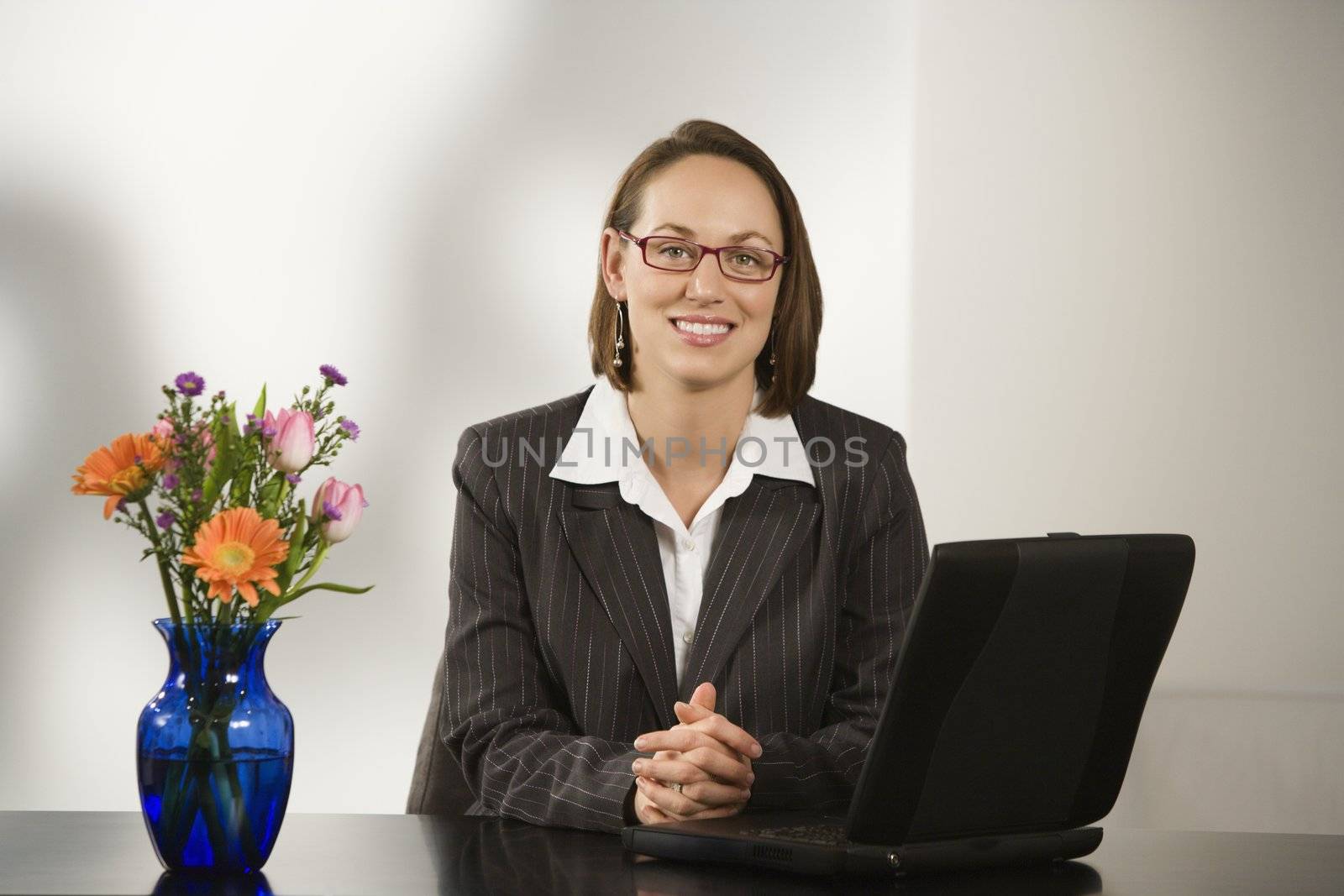 Caucasian businesswoman sitting at desk smiling with laptop computer.