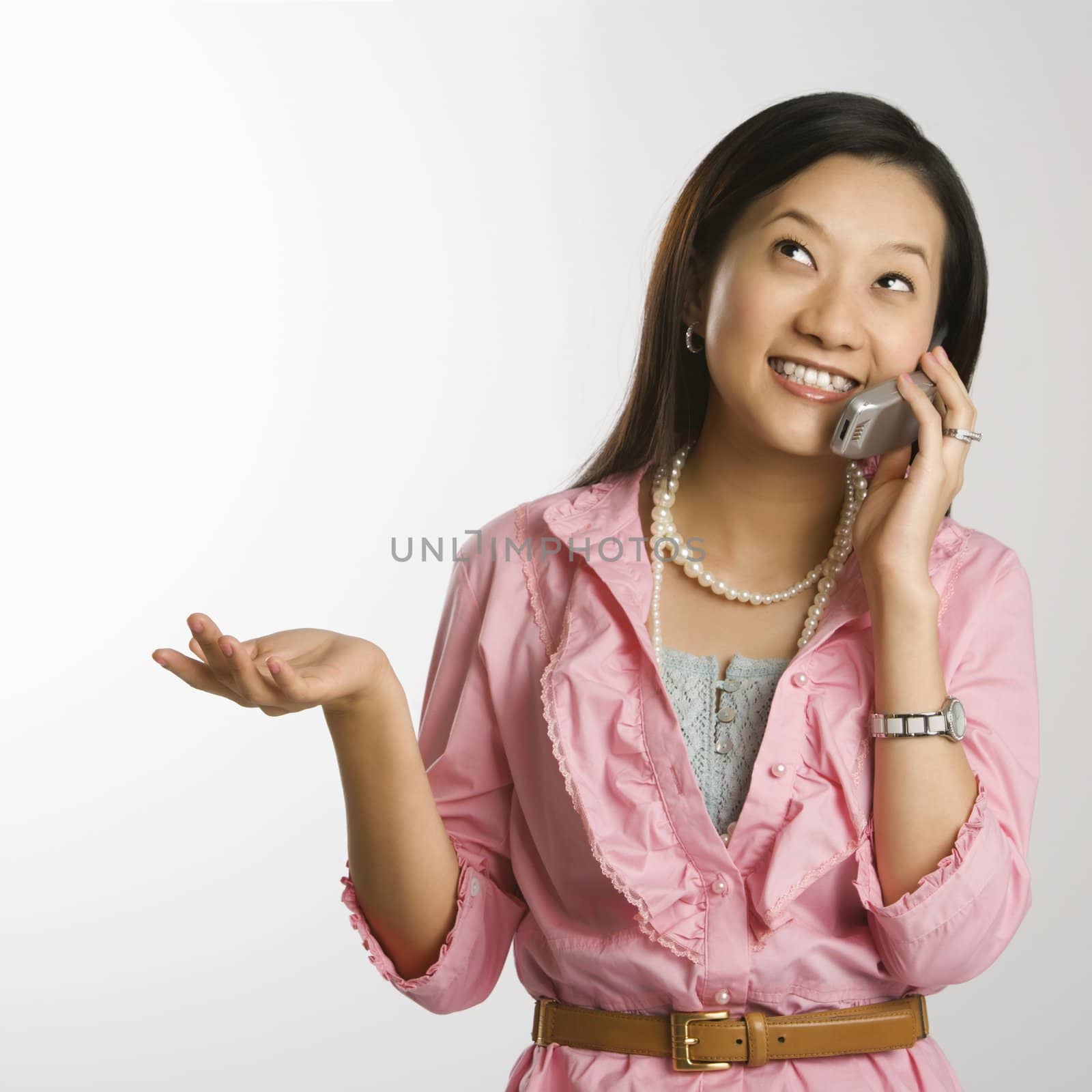 Portrait of Asian Chinese mid-adult female with hand out, looking up, smiling and talking on cell phone.