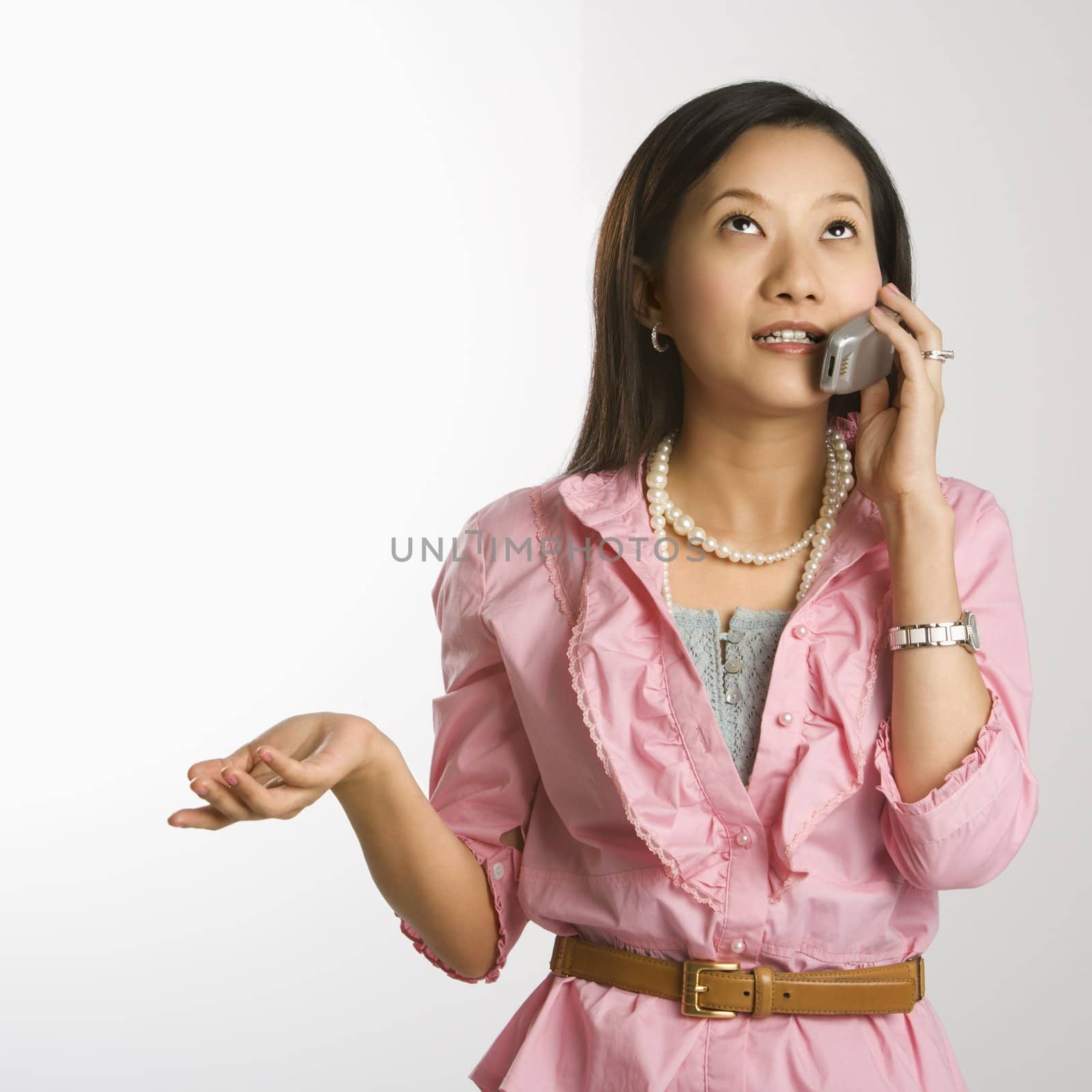 Portrait of Asian Chinese mid-adult female with hand out, looking up and talking on cell phone.
