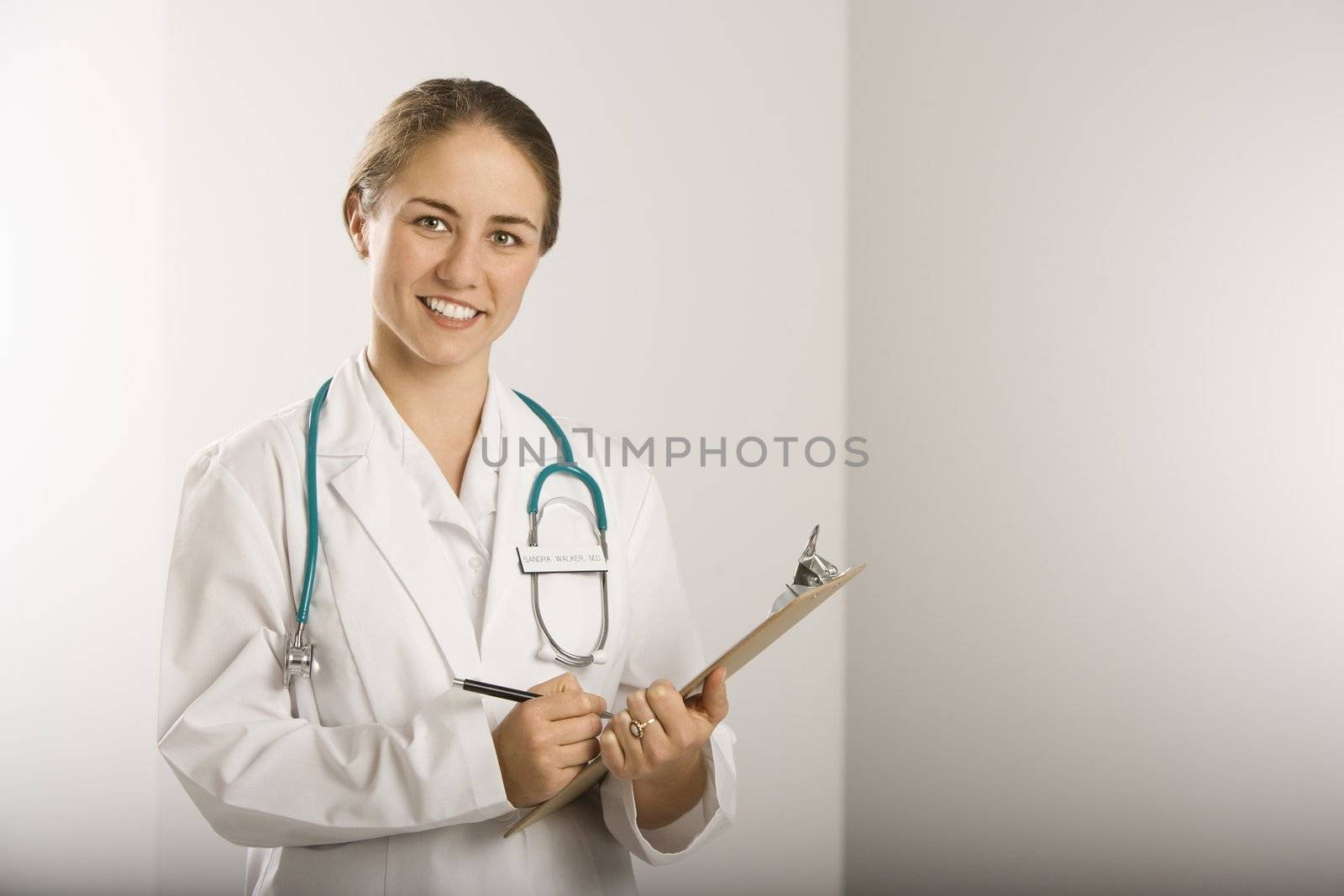 Portrait of Caucasian mid-adult female doctor writing on clipboard, smiling and looking at viewer.