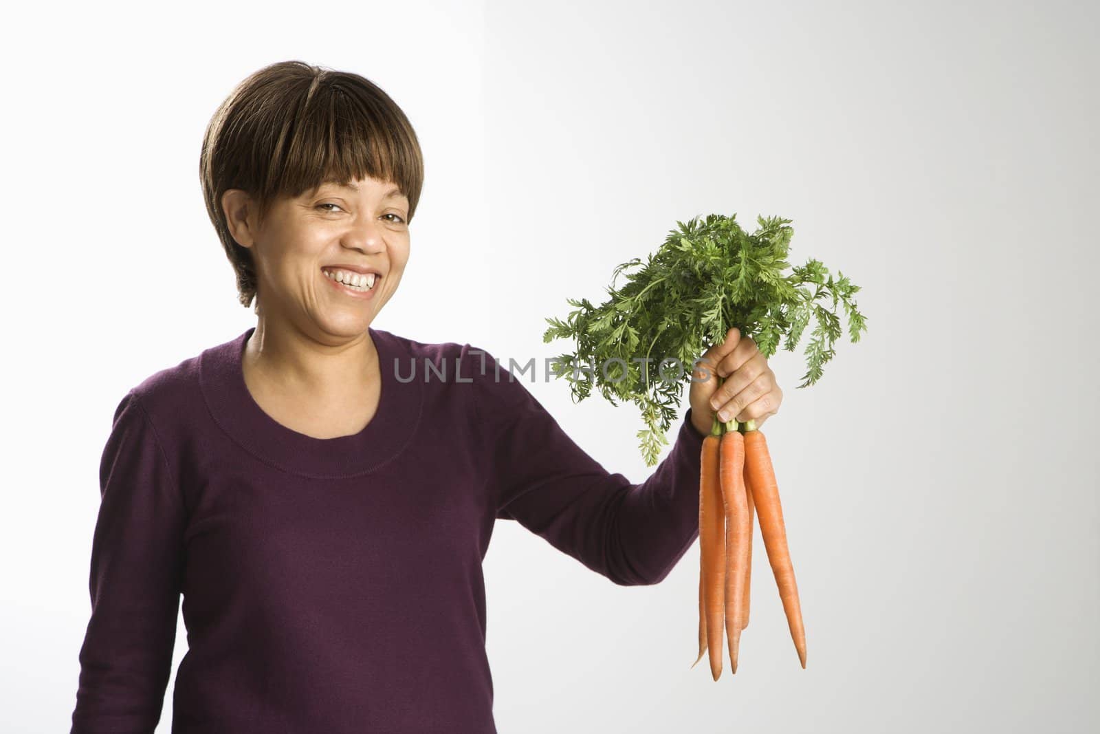 Portrait of African American middle-aged woman holding bunch of fresh carrots smiling and looking at viewer.