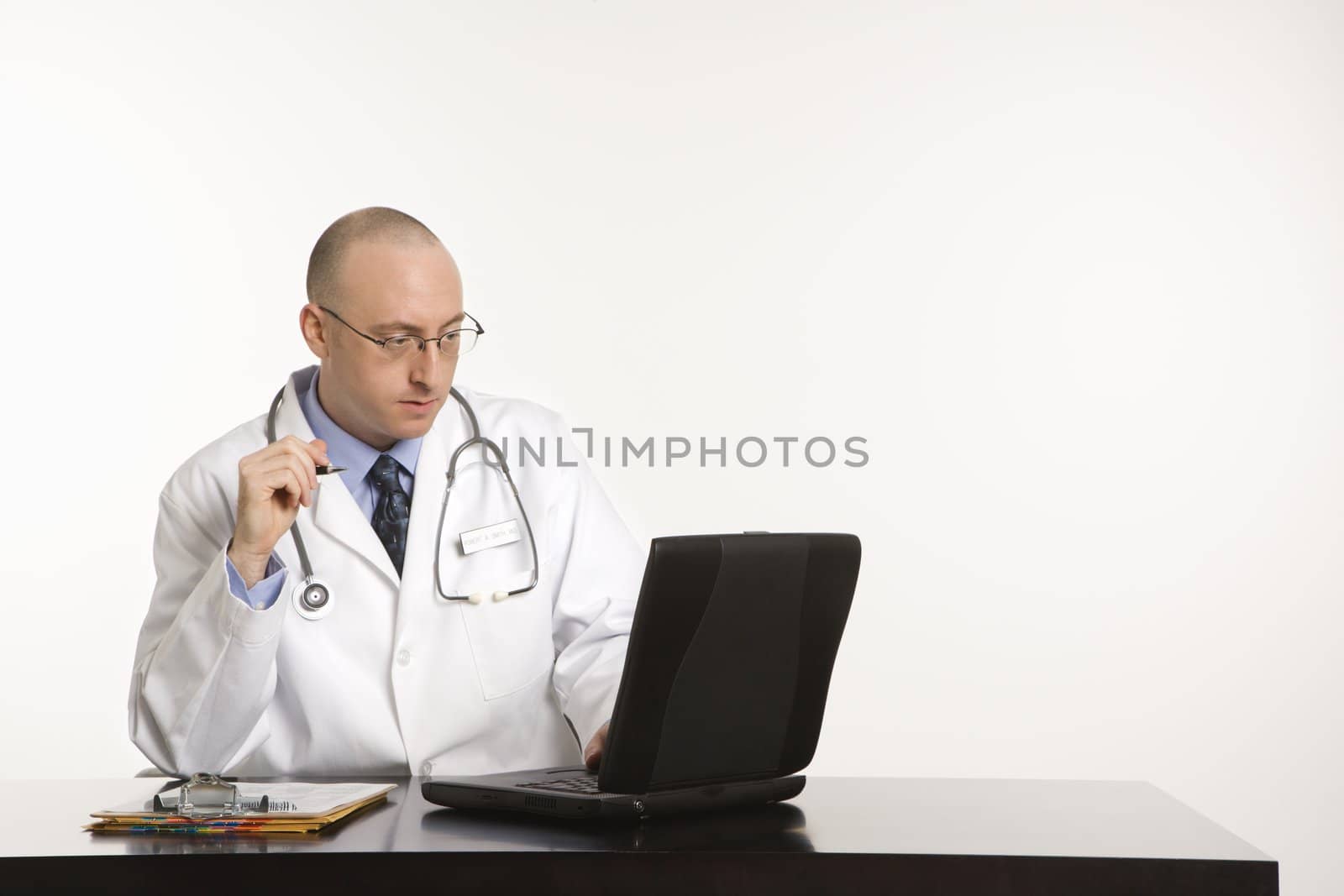 Caucasian mid adult male physician sitting at desk with laptop computer.