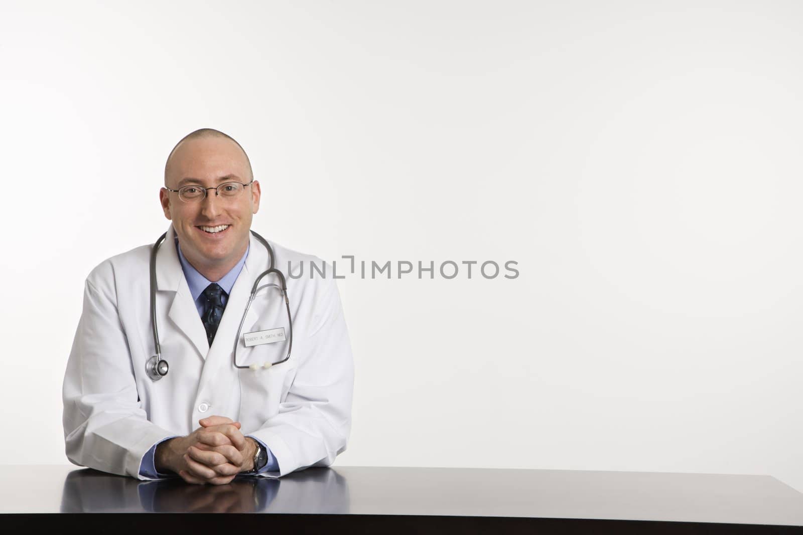 Caucasian mid adult male physician sitting at desk smiling.