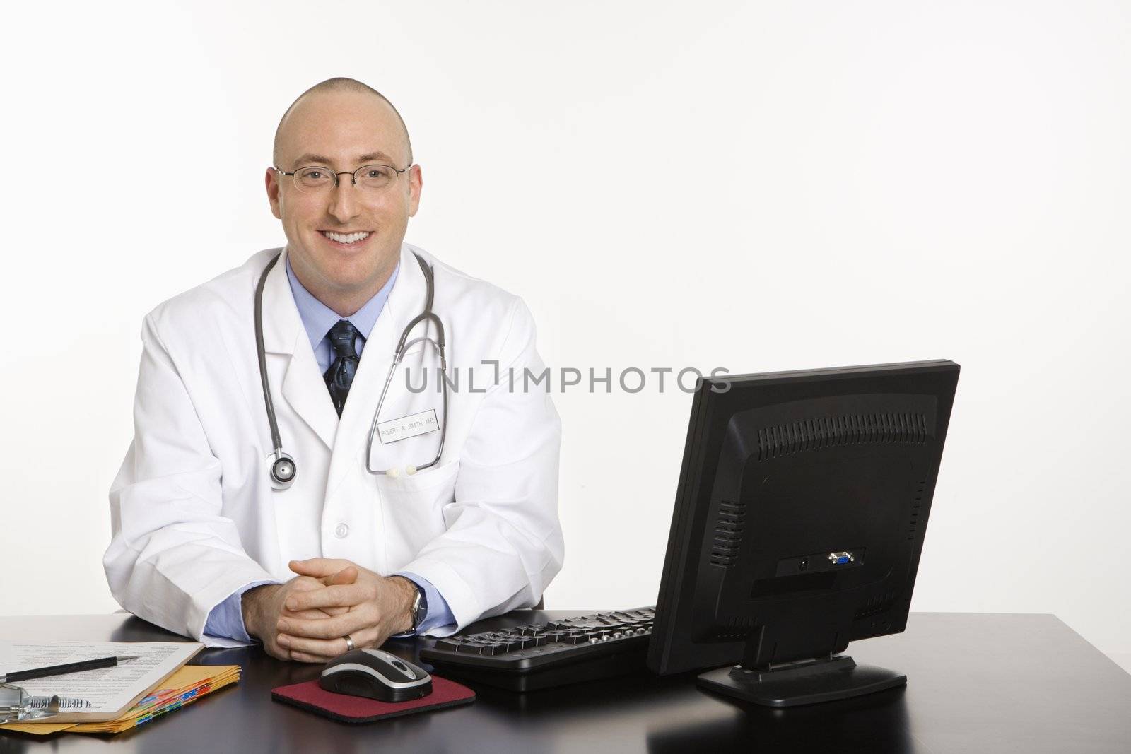 Caucasian mid adult male physician sitting at desk smiling with laptop computer.