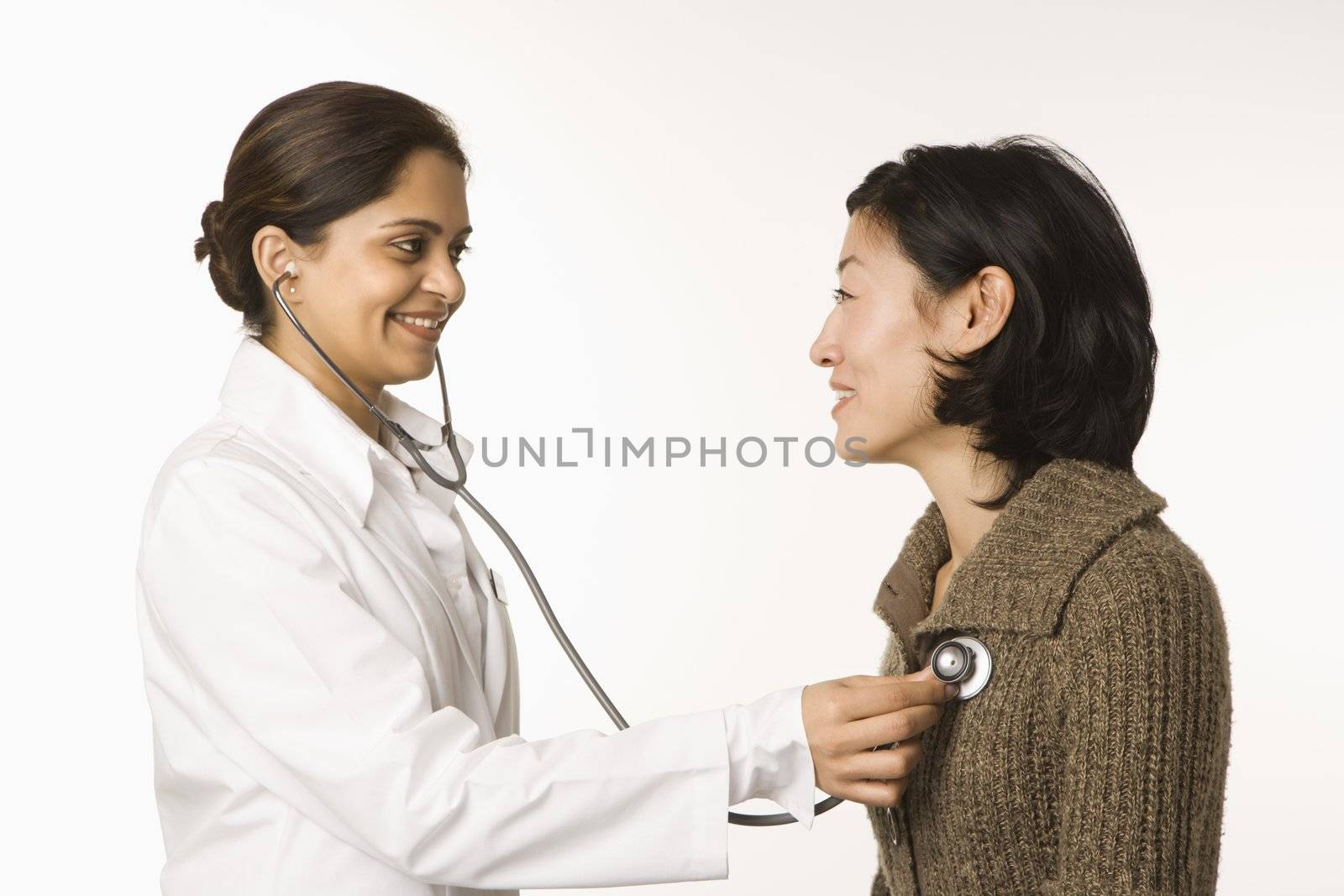 Indian woman doctor using stethescope on Asian woman patient.