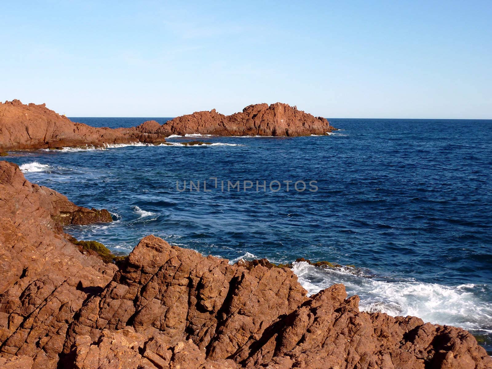 Red rocks and blue mediterranean sea with waves at the Esterel massif, south of France, by beautiful weather