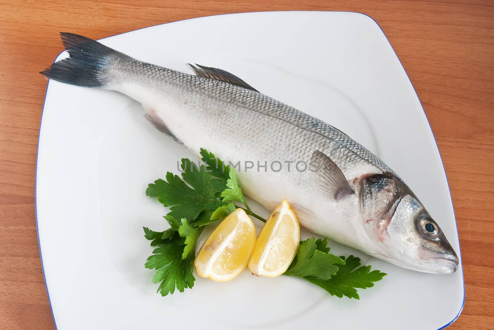 plate with sea bass, lemon and parsley isolated on wooden background