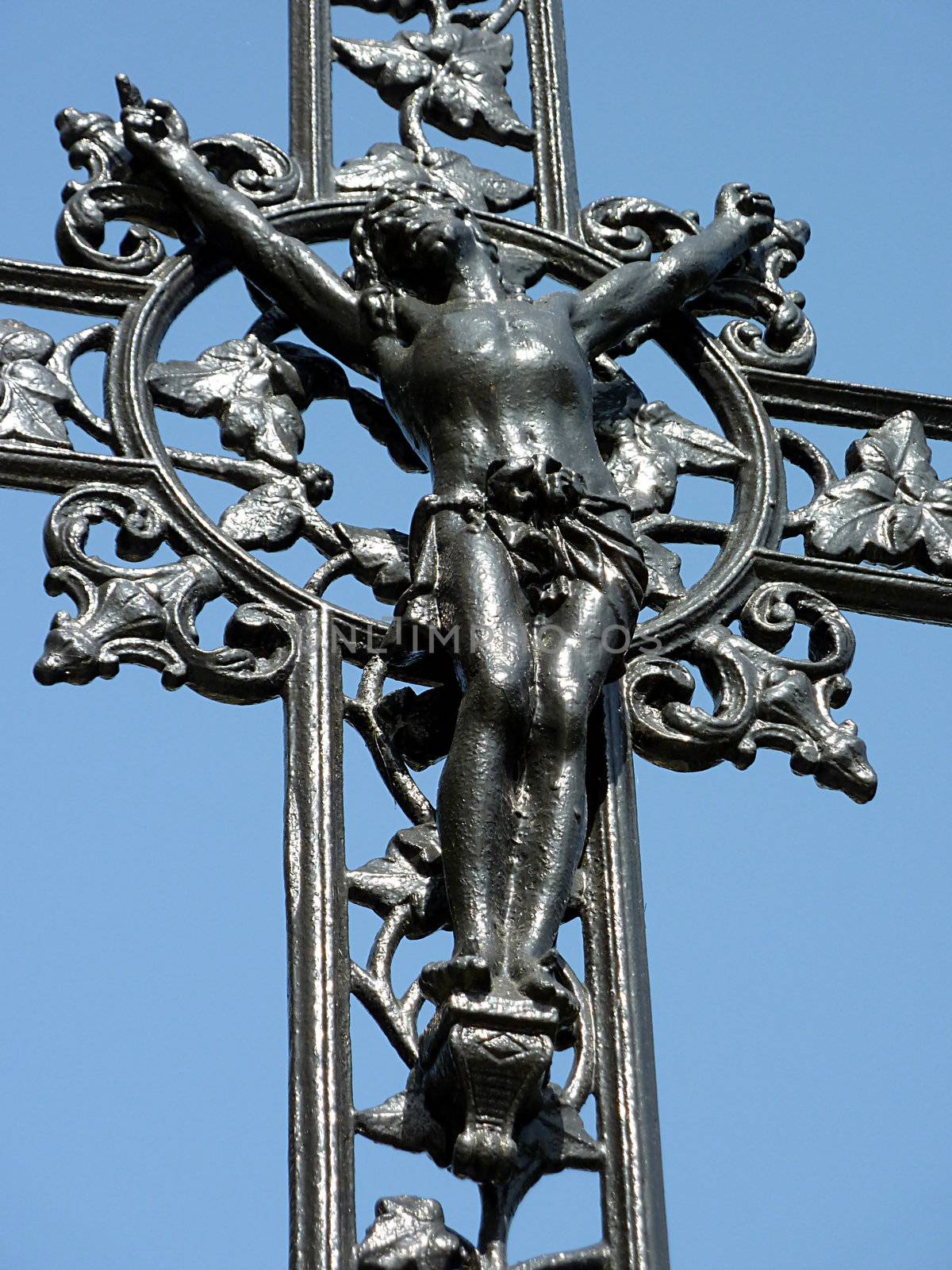 Jesus cross made of black metal with lots of decorations around and blue sky behind