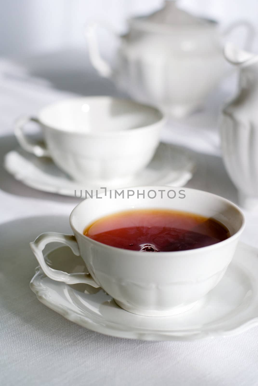 Tea set - two teacups, one with steaming hot tea, sugarbasin behind. Focus on teacup, shallow depth of field.