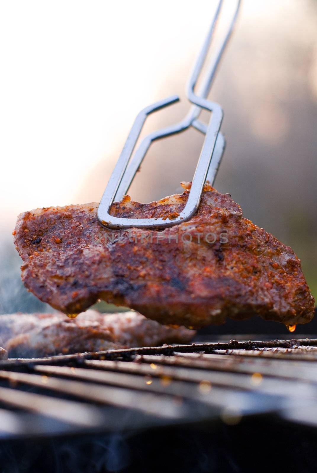 Delicious chuck steak on the grill in metal tongs. Shallow depth of field.