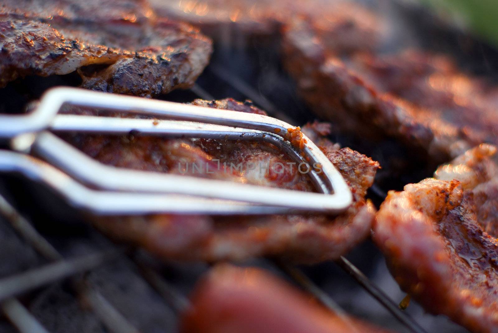 Delicious chuck steaks on the grill - detail with metal tongs. Shallow depth of field.