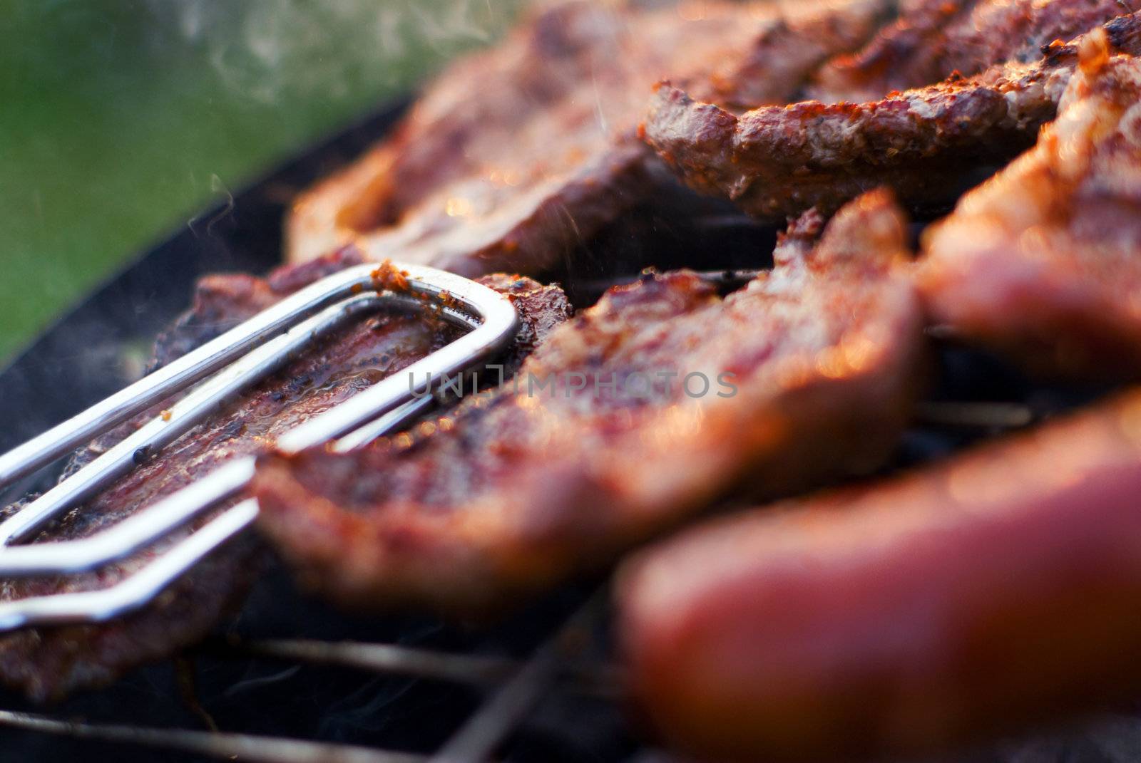 Delicious chuck steaks on the grill - detail with metal tongs. Shallow depth of field.