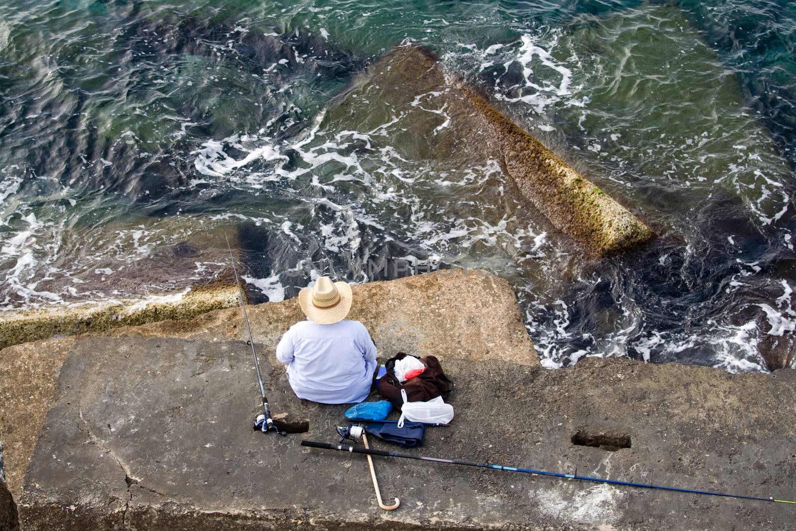 Fisherman in hat is sitting on the stone and fishing, top horizontal view