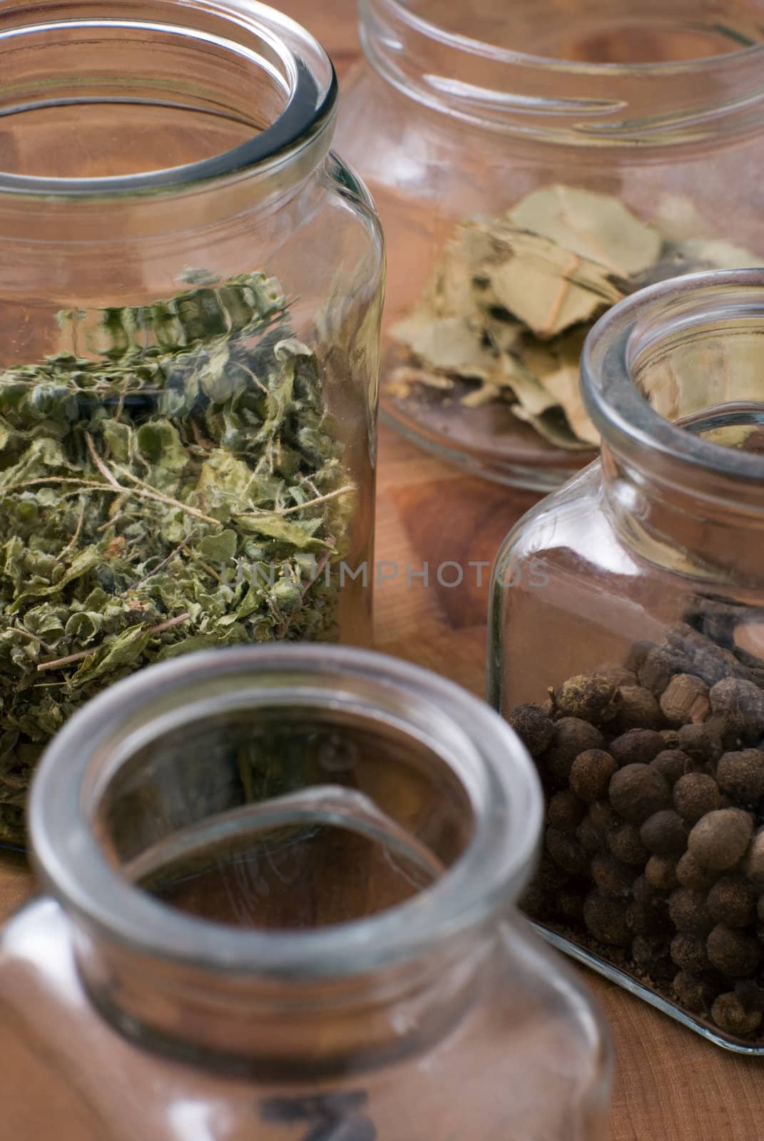 Glass jars with herbs - allspice, dried bay leafs and marjoram or oregano or other green.