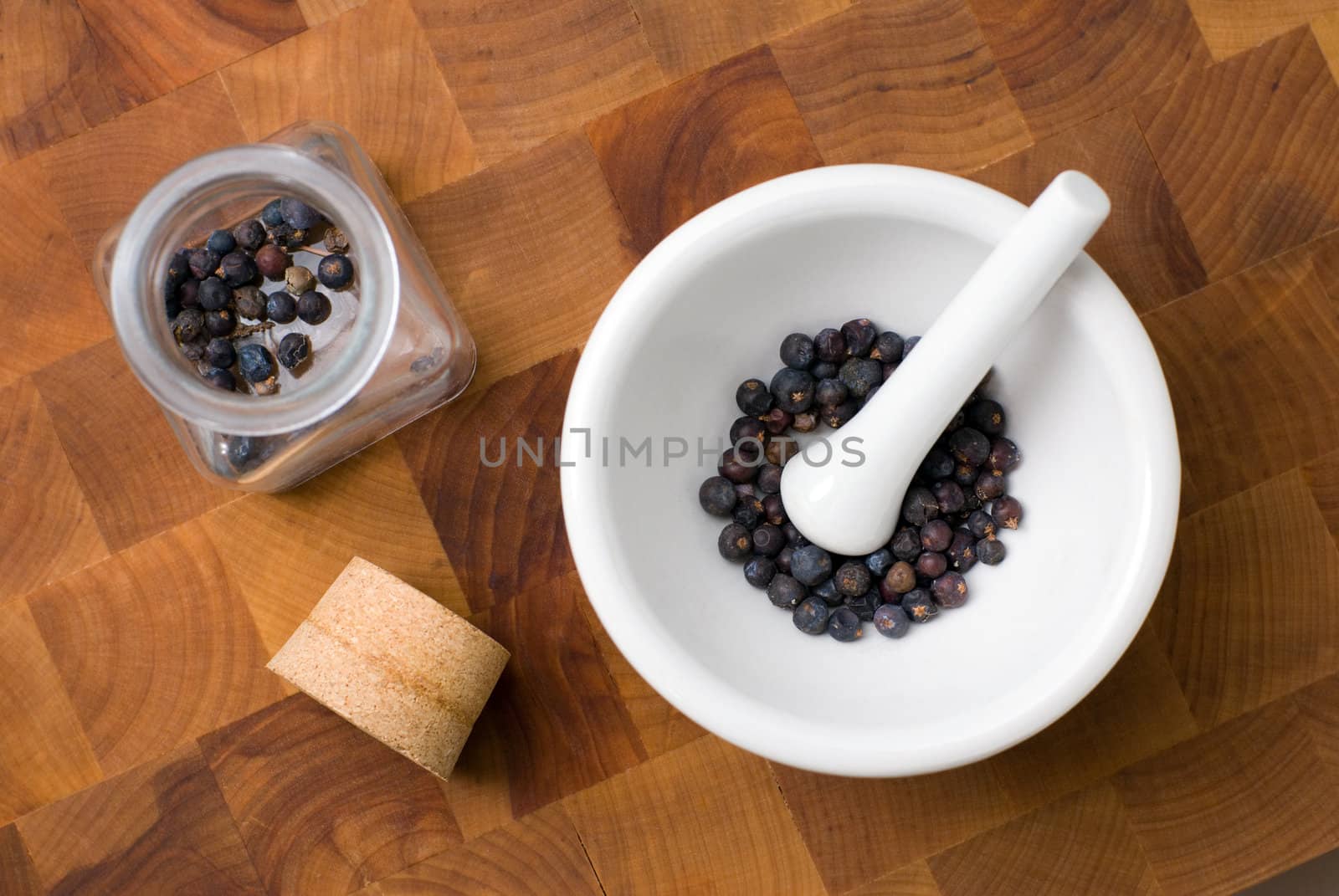 Juniper in ceramic mortar and pestle and glass jar with cork on the cutting board.