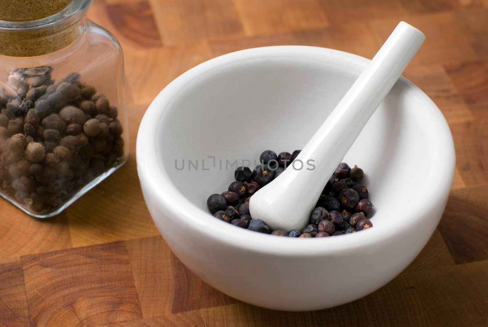 Juniper in ceramic mortar and pestle and glass jar with allspice on the cutting board.