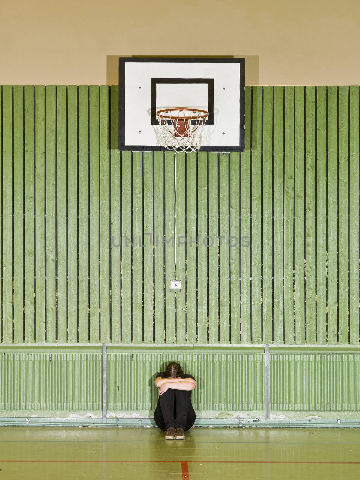 Sad girl sitting under a basket hoop