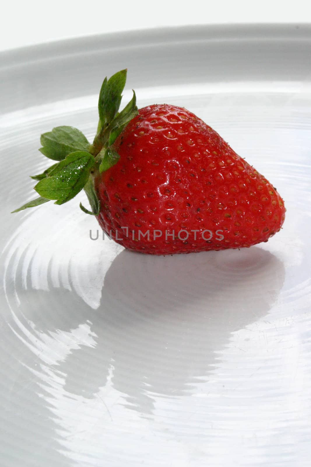 An isolated red strawberry on white dish
