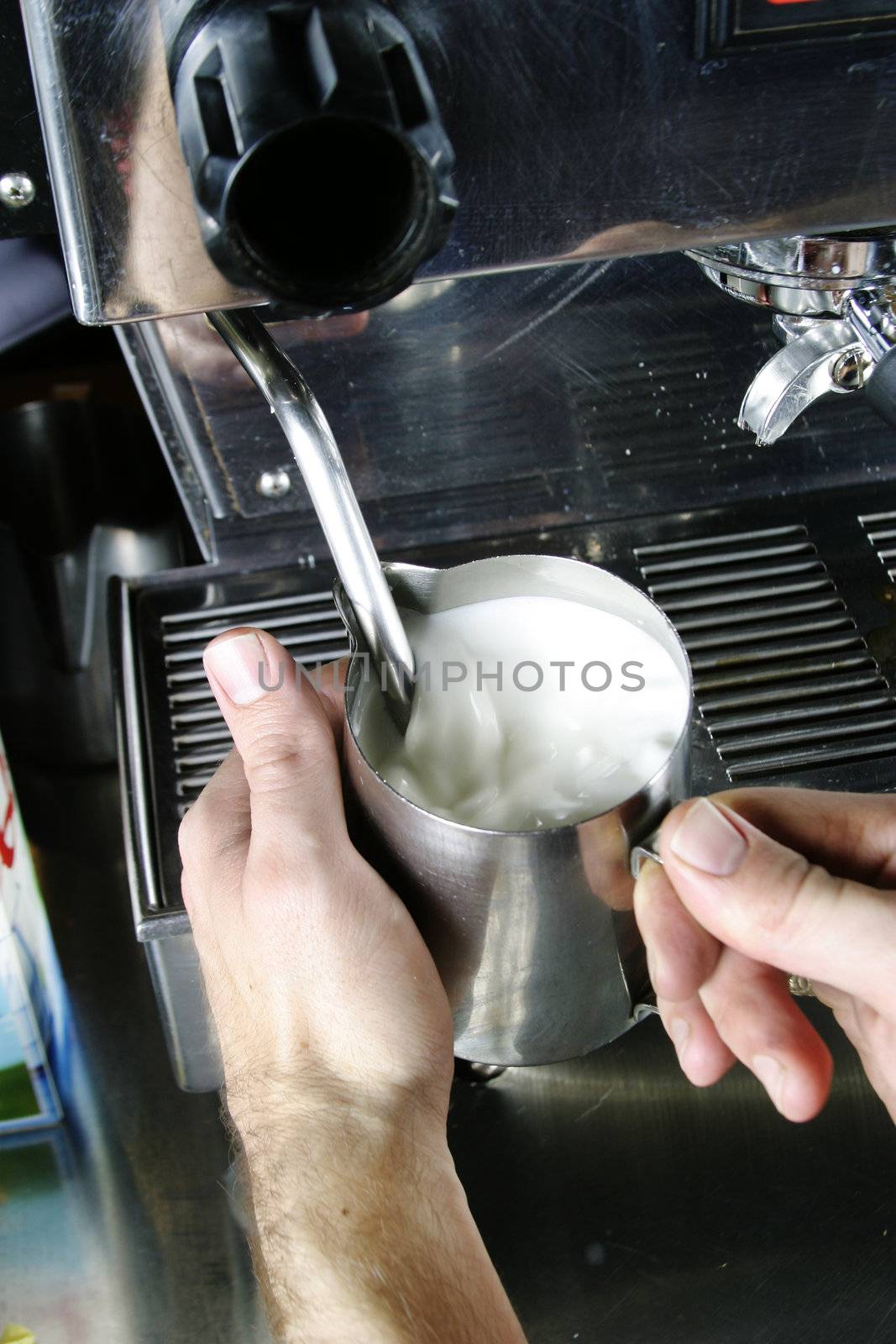 A professional barista is steaming milk for a cafe latte