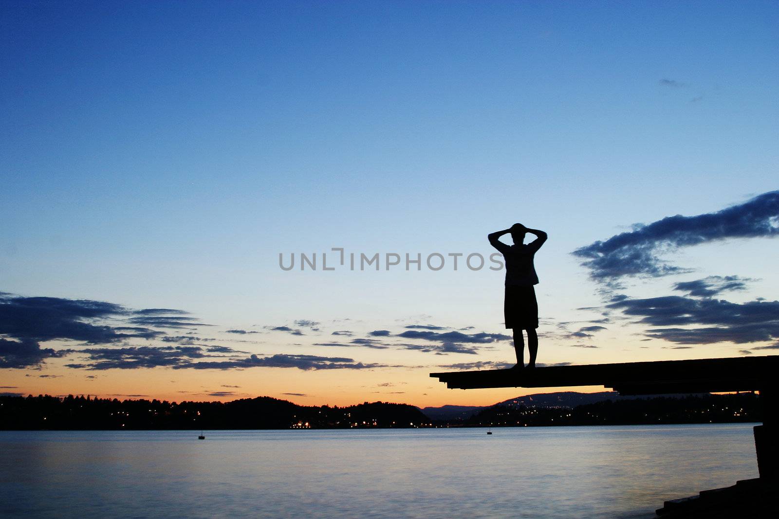 A young person sitting on a dock at dusk, at the fjord in Oslo, Norway