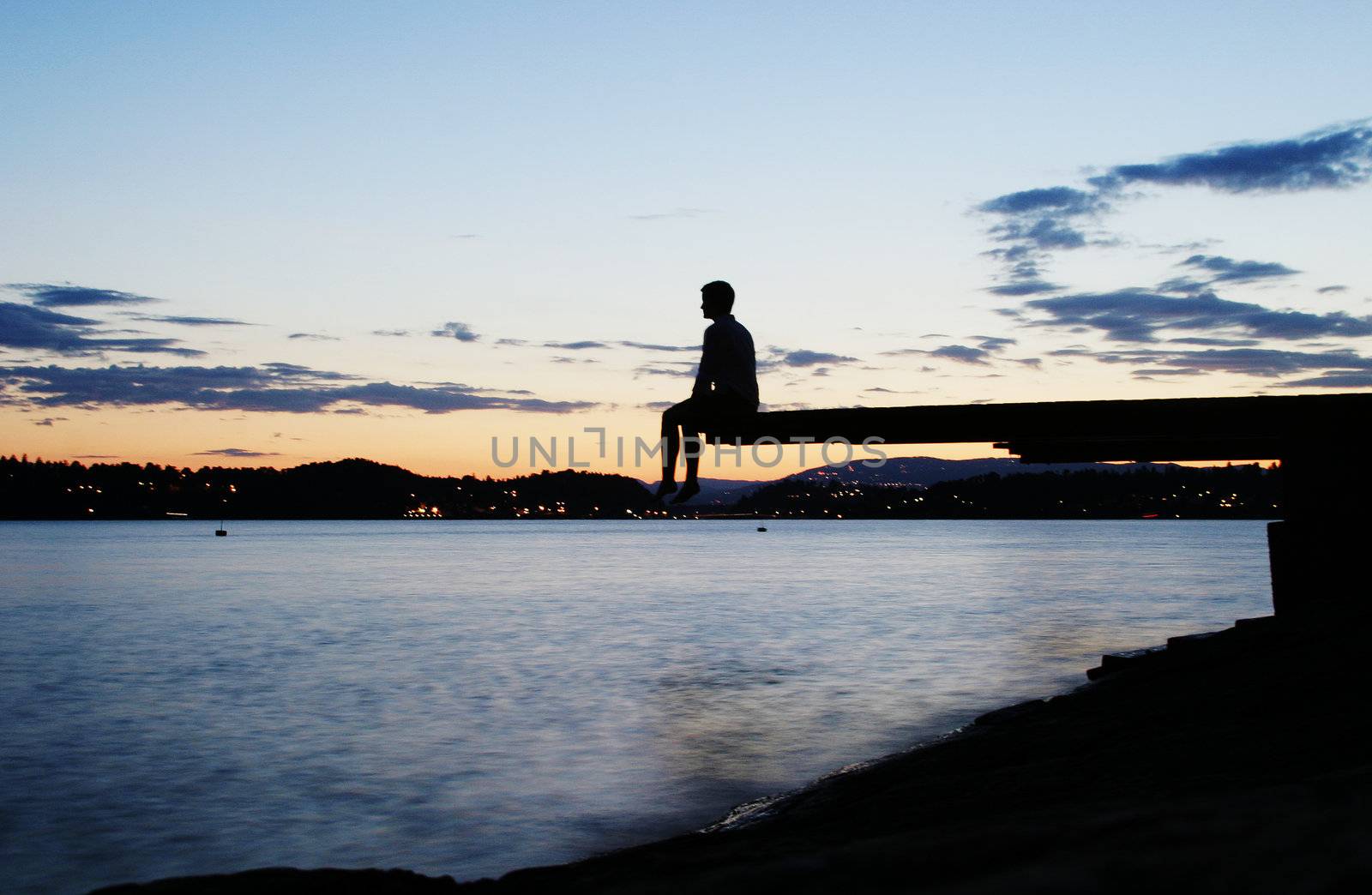 A young person sitting on a dock at dusk, at the fjord in Oslo, Norway