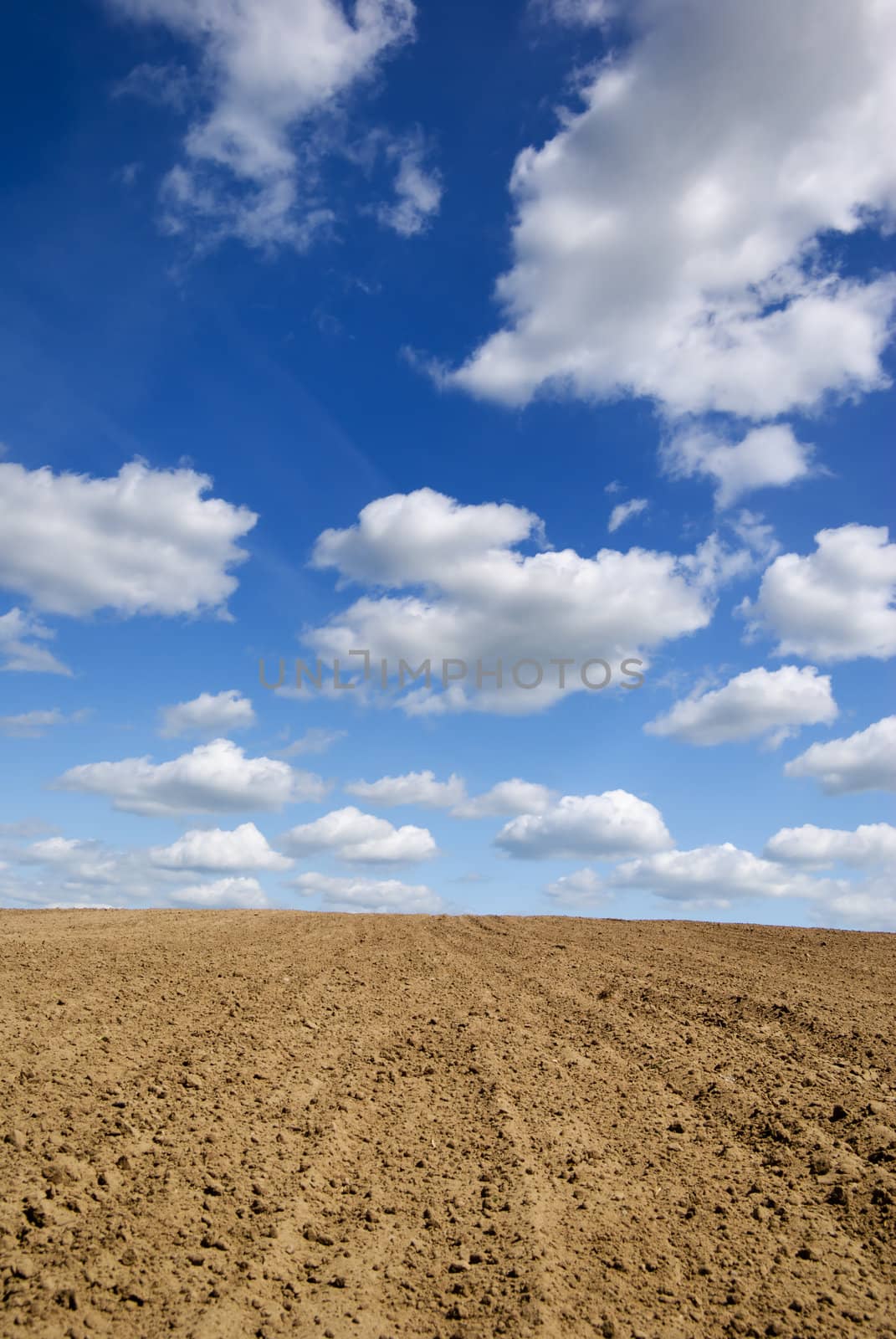 Blue sky with clouds over ploughed field.