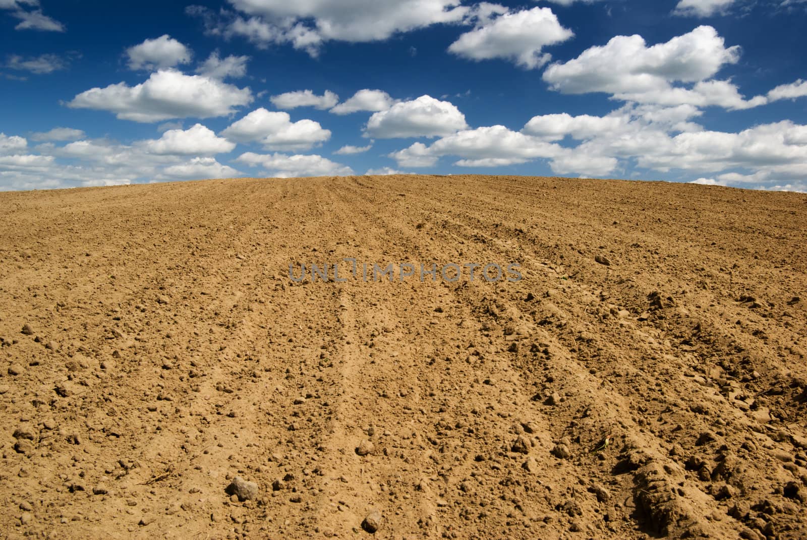 Blue sky with clouds over ploughed field.