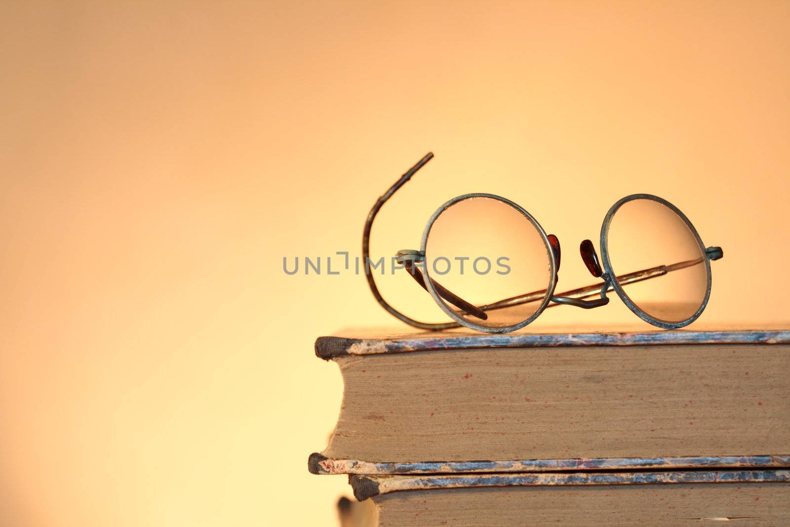 Old spectacles lying on ancient books isolated on yellow background