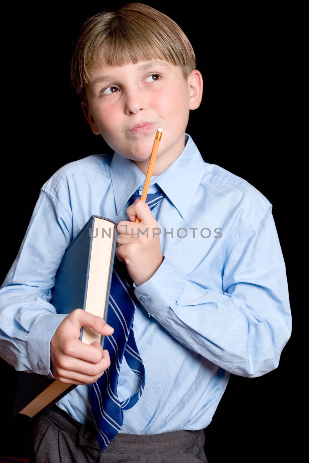 A school boy student in uniform holding textbook and pencil and thinking.  Dark background.