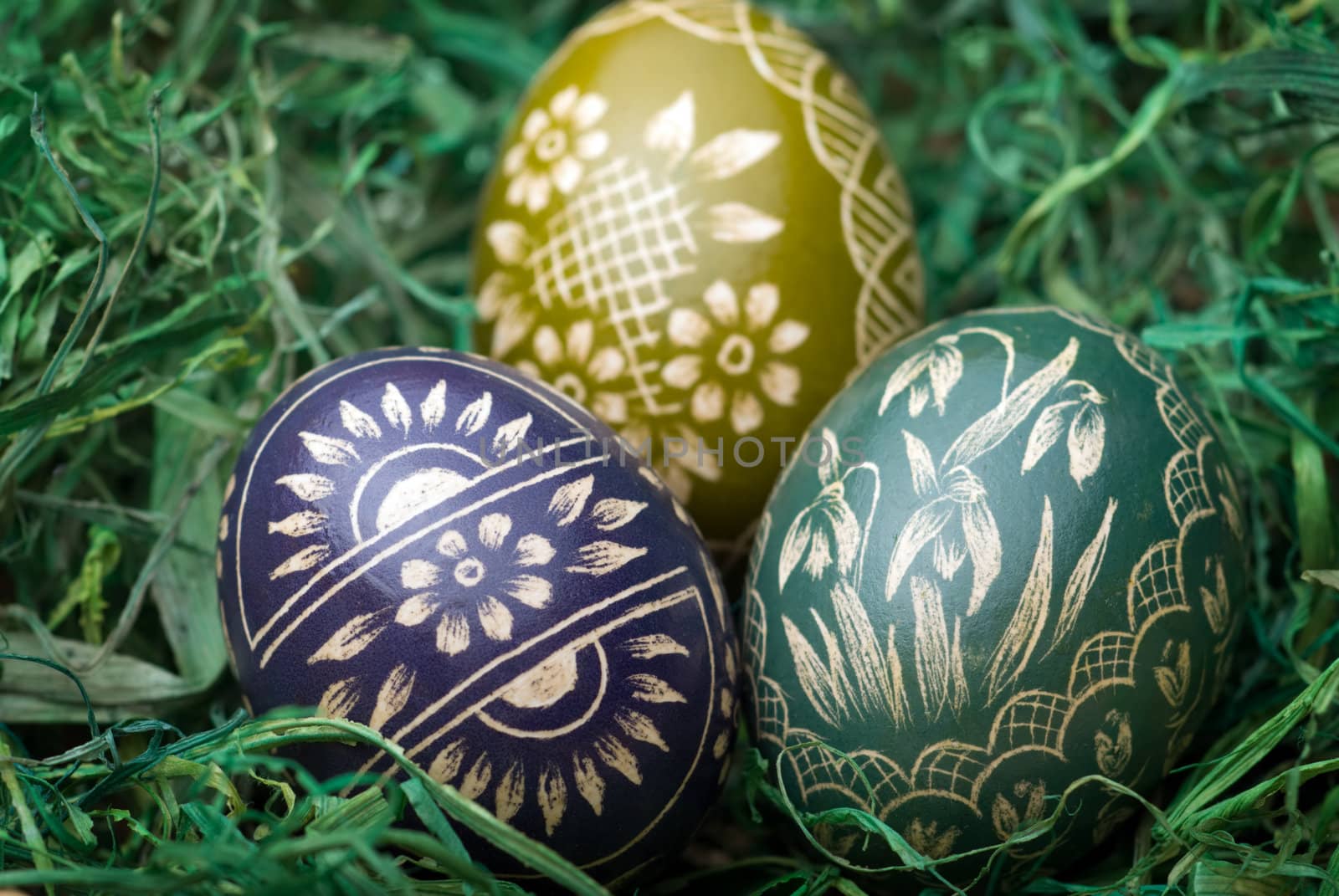 Three handmade easter eggs on the green hay. Selective focus, shallow depth of field.
