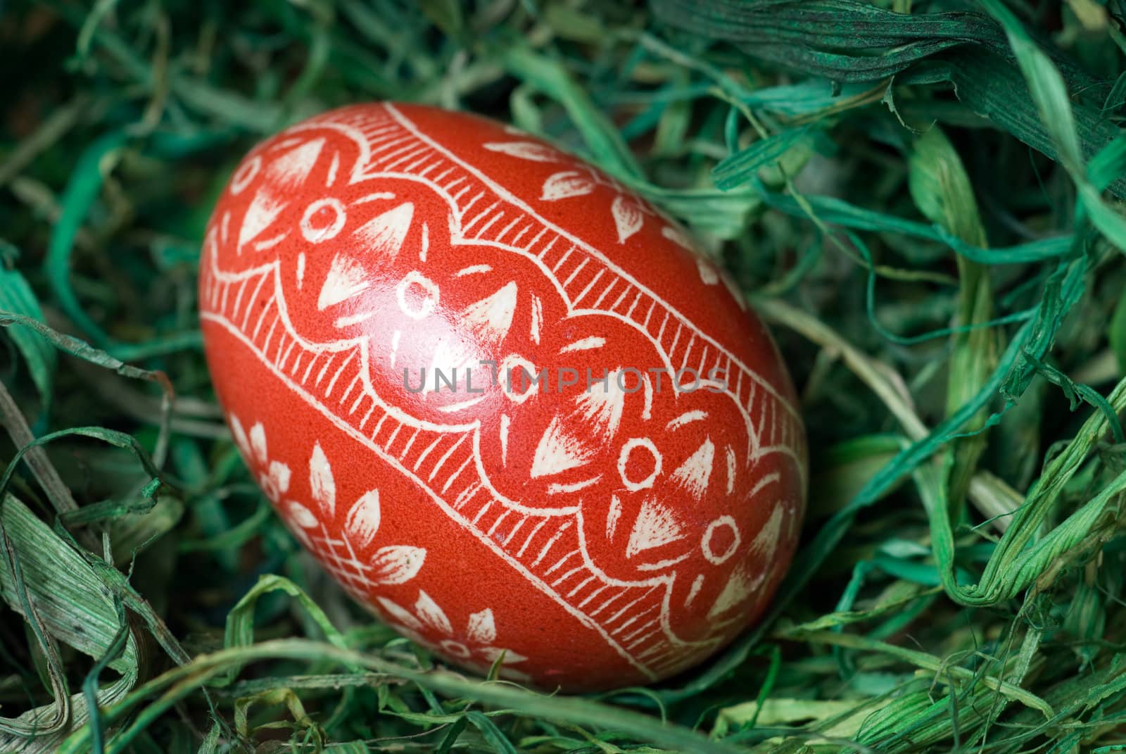 Handmade easter egg on the green hay. Shallow depth of field.