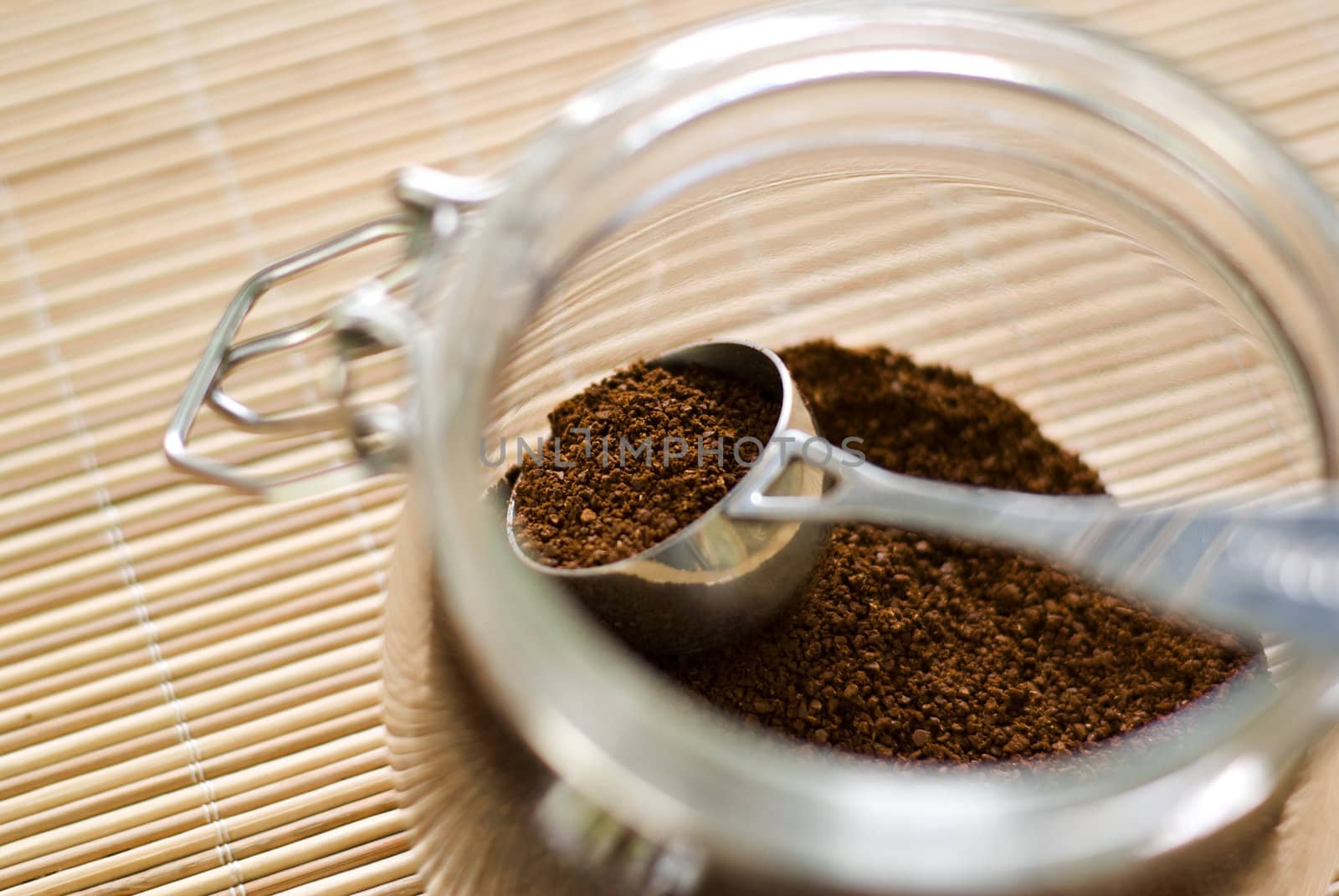 Coffee scoop filled with ground coffee (focus on it) in the glass jar. Shallow depth of field.