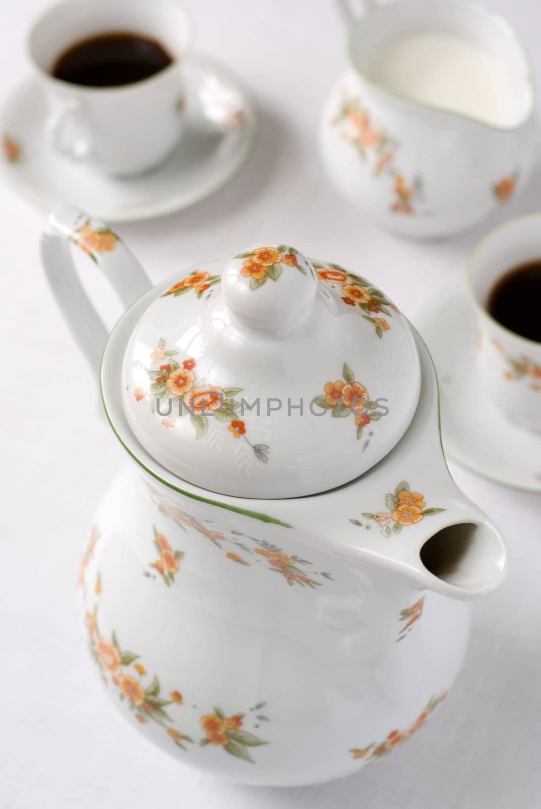 Coffee or tea set on the table - teapot on the front (focus on the top of it) cups and milk jug behind. Shallow DOF.