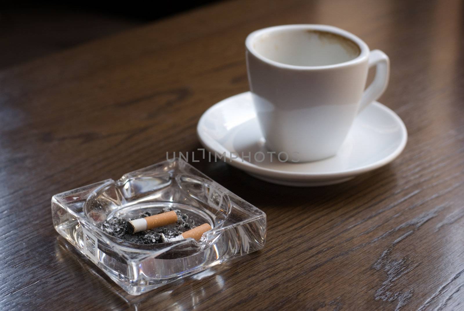 Ashtray and empty coffe cup on the cafe table. Shallow depth of field (focus on the cigarette butt).