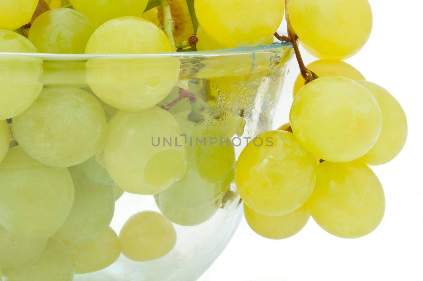 Close and low level capturing a glass bowl filled with green grapes and arranged over white.