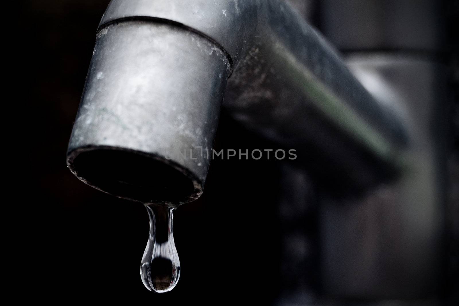 An old leaky faucet with focus on a drop of water, meaning the waste of water in the world.
