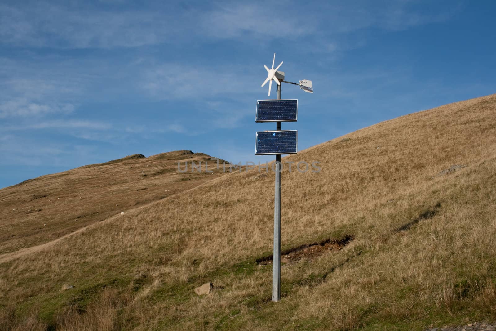 Wind turbine and solar panel combination on mountain side.