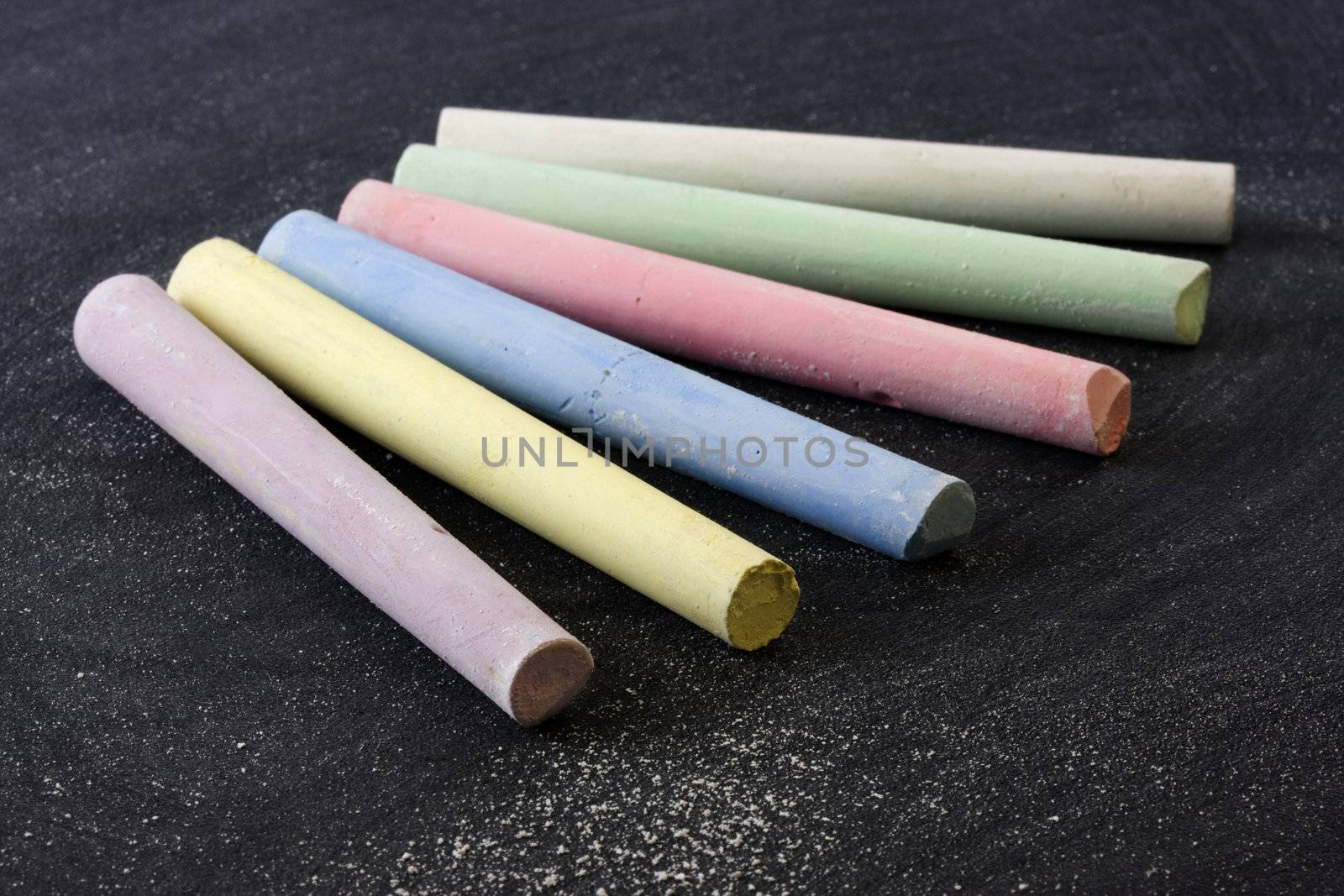 6 pieces of chalk in different color on balckboard with dust and eraser smudges