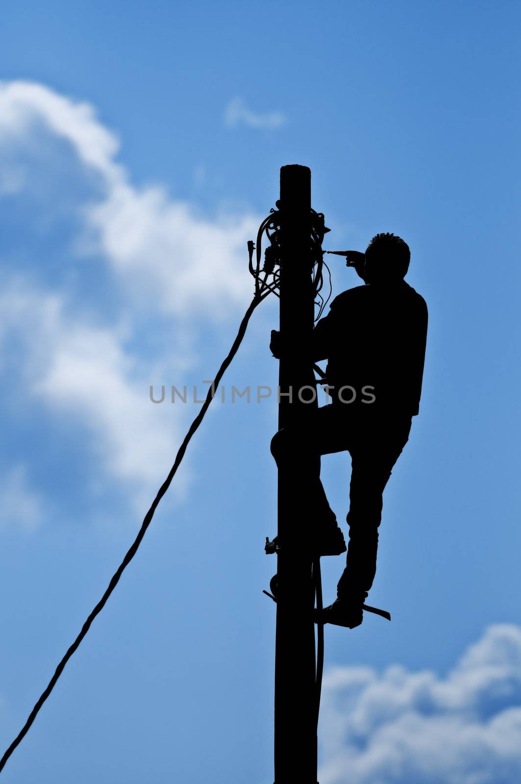 Silhouette of the man repairing wires on the pole