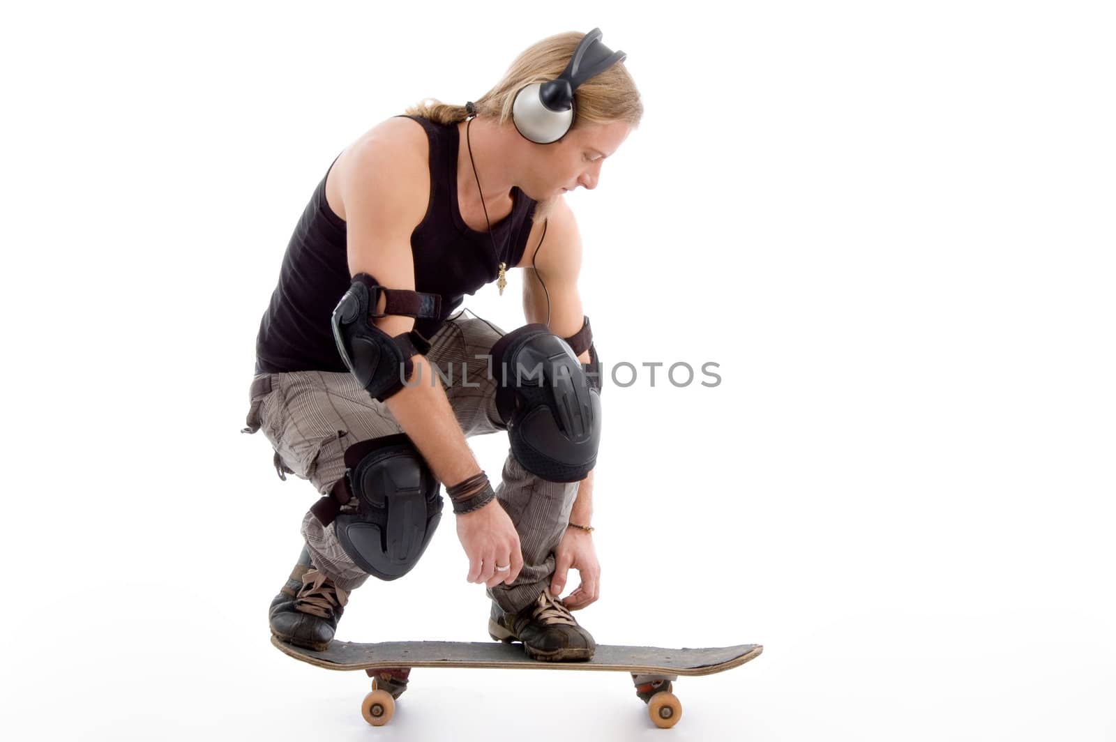 handsome guy tying his shoes laces and sitting on skateboard with white background