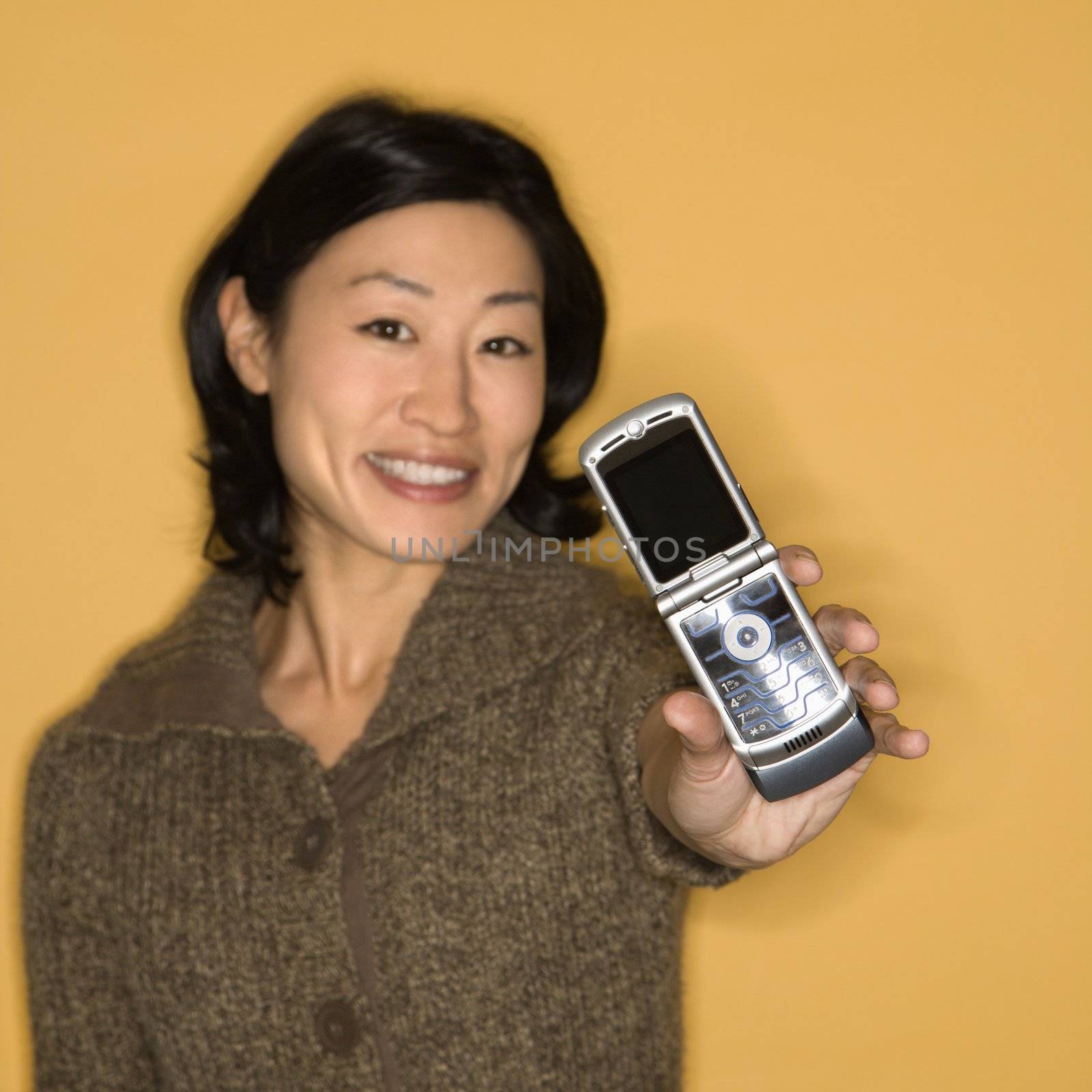 Pretty mid adult Asian woman holding out cell phone.
