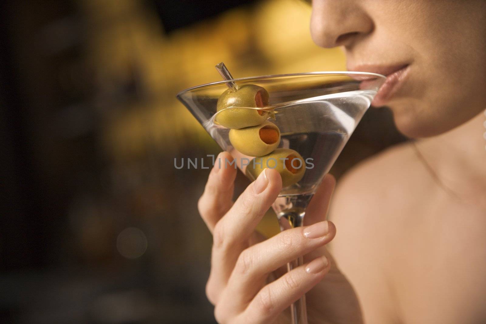 Close up of mid adult Caucasian woman drinking a martini with three olives.