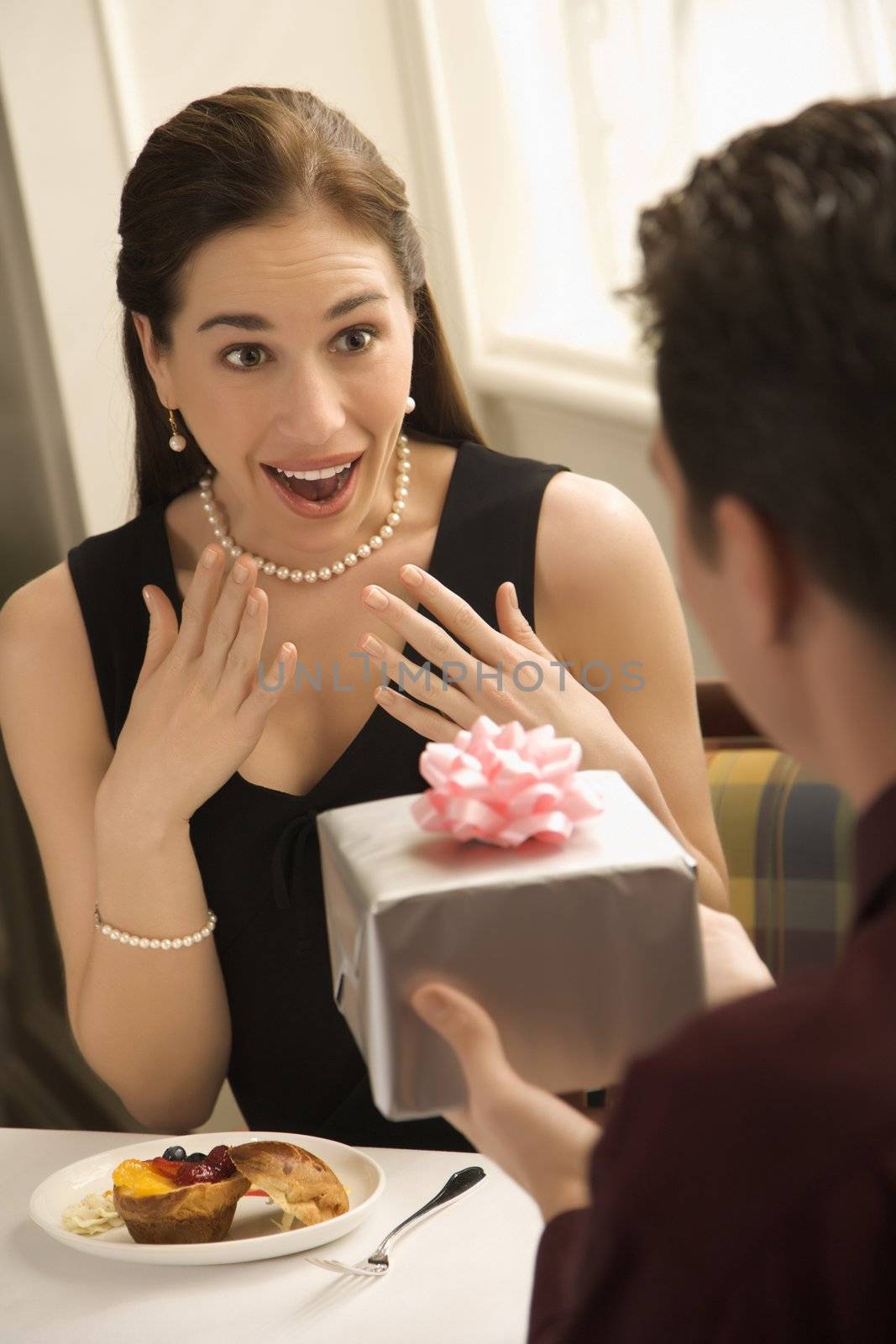 Mid adult Caucasian man presenting wrapped gift to surprised woman at restaurant.