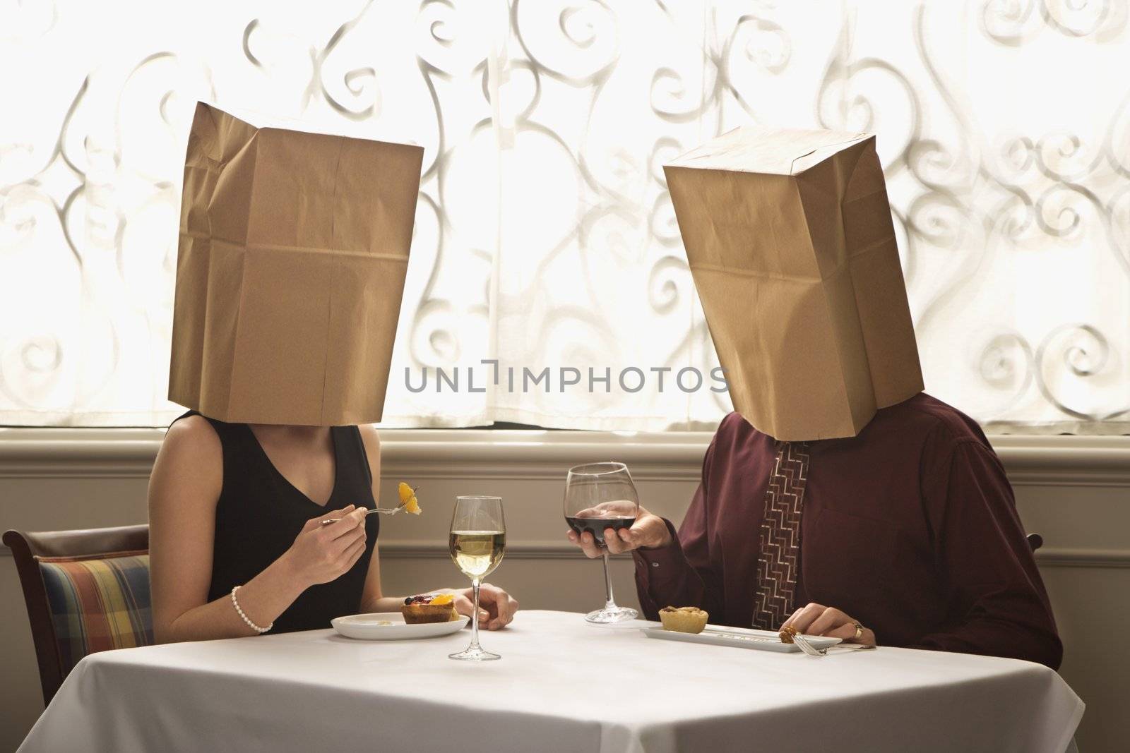 Mid adult Caucasian couple dining in a restaurant with paper bags over heads.