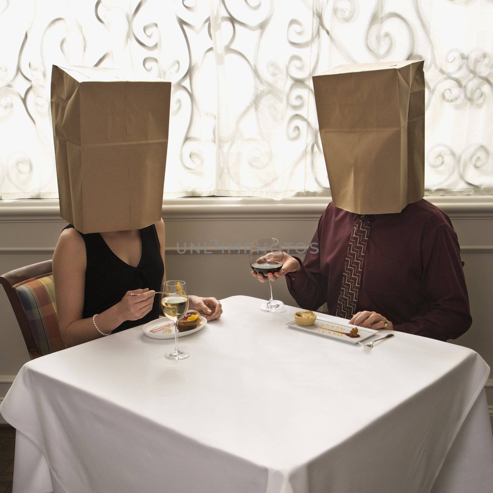 Mid adult Caucasian couple dining in a restaurant with paper bags over heads.