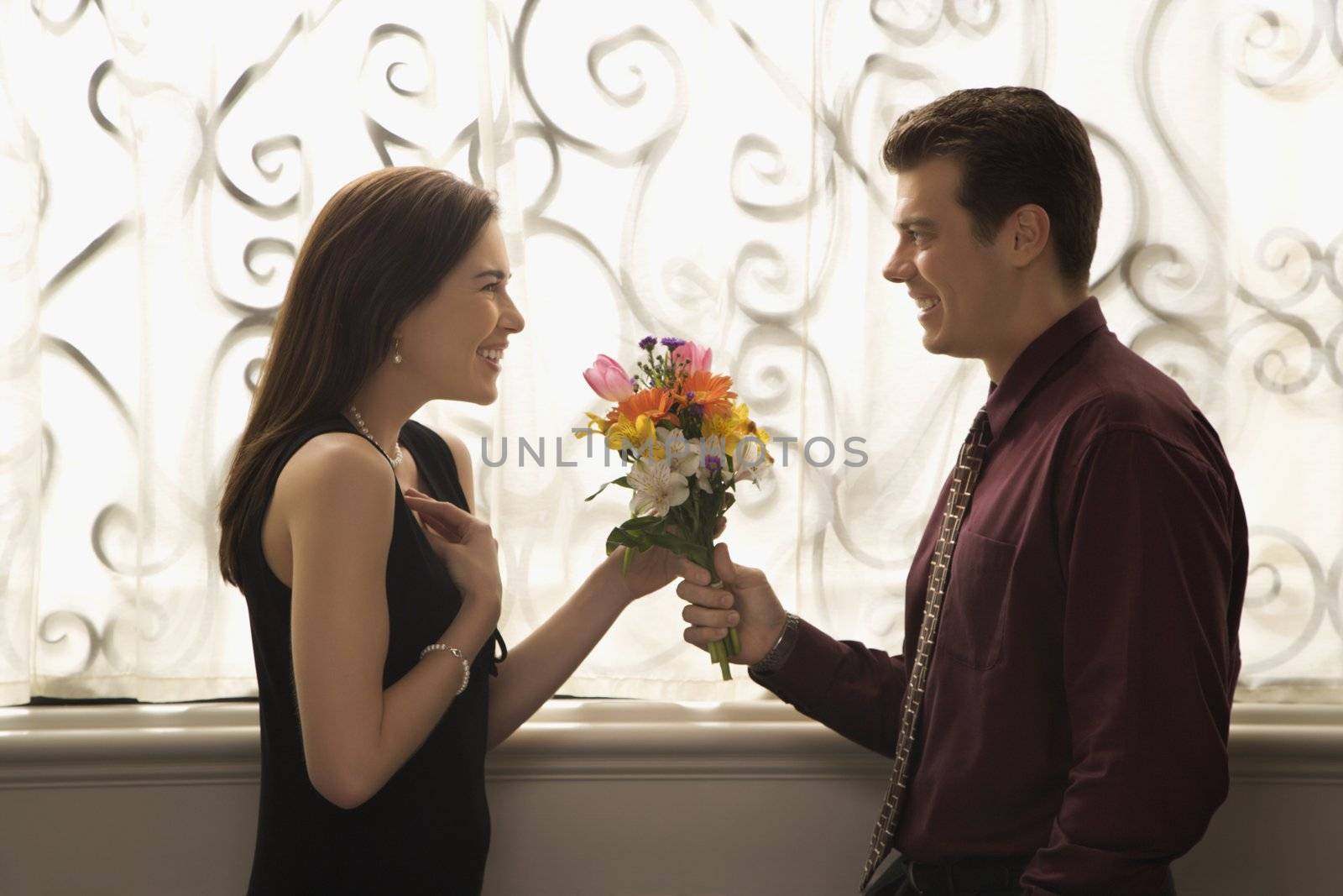 Mid adult Caucasian man presenting surprised woman with bouquet of flowers.