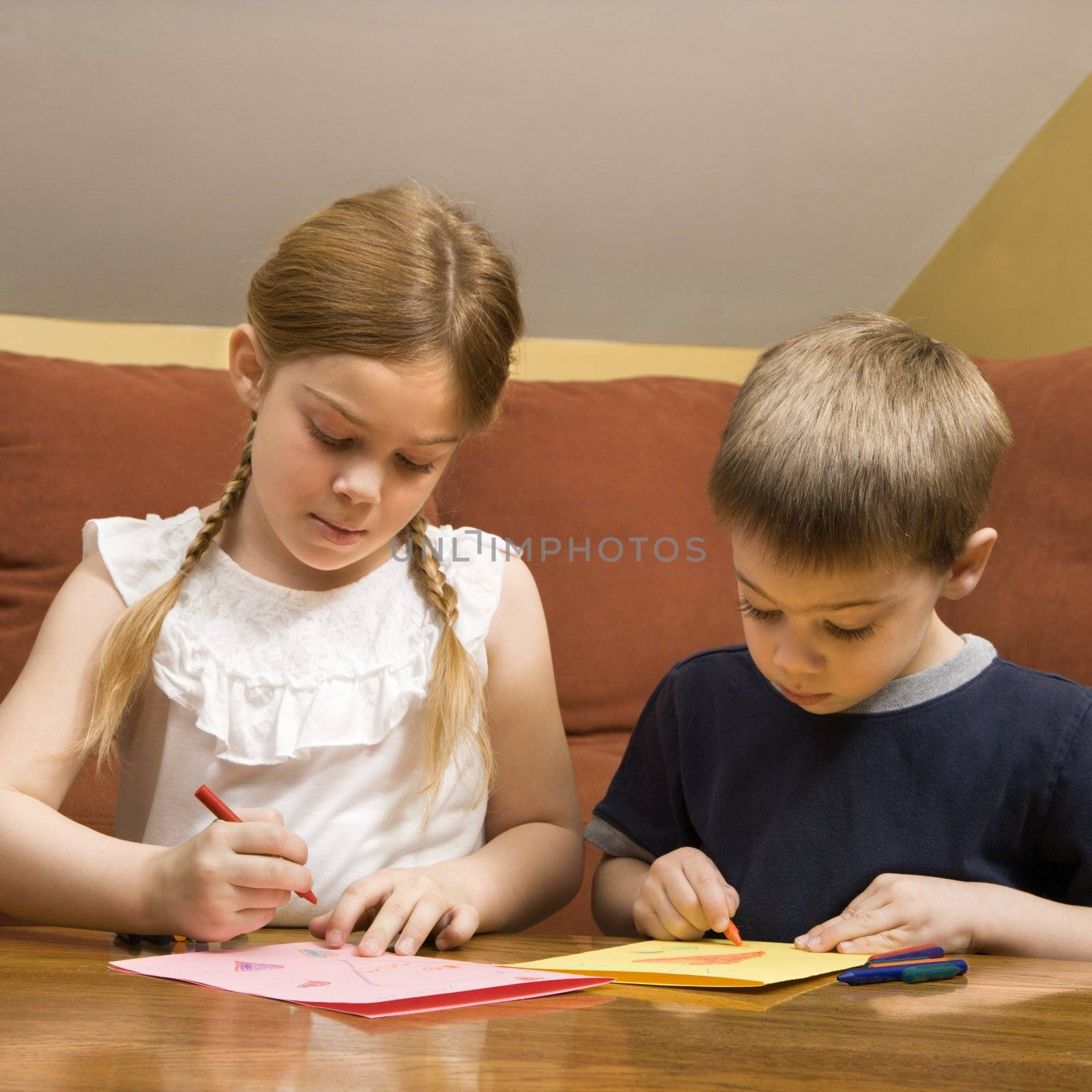 Caucasian boy and girl drawing on paper with crayons.