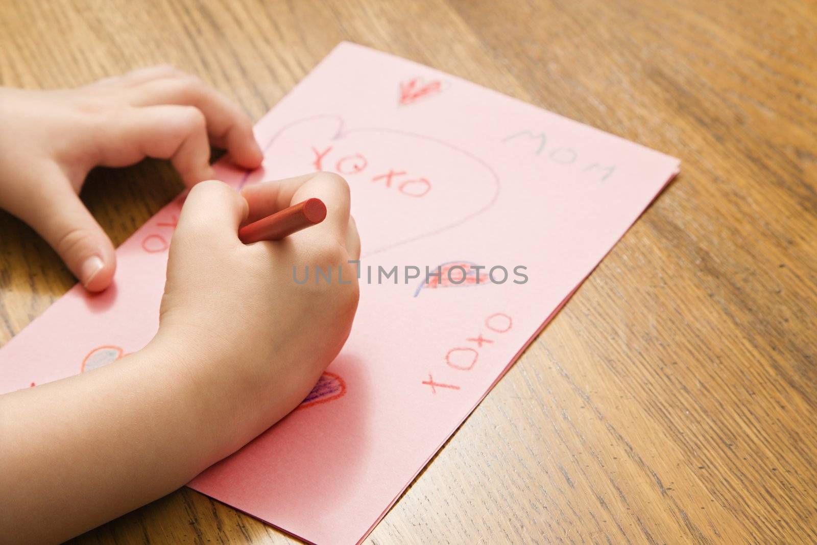 Caucasian female child hands drawing on paper with crayons.