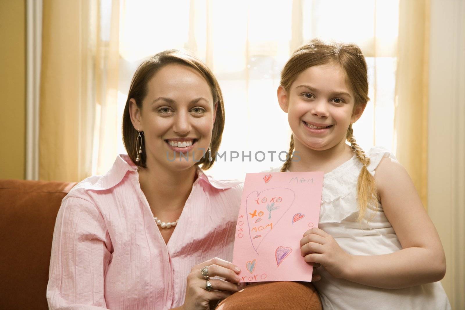 Caucasian girl giving mid adult mother a drawing and looking at viewer.