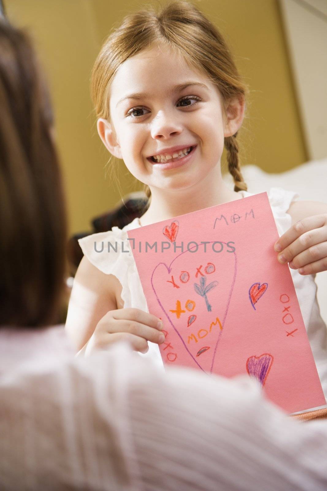 Caucasian girl giving mid adult mother a drawing.